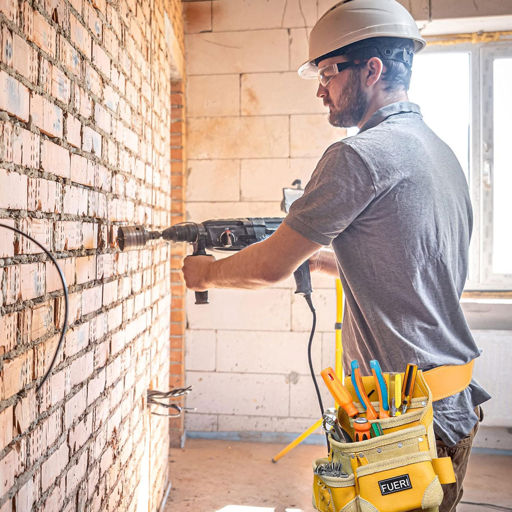 An electrician standing, helmet on head, drilling in the wall, wearing Fueri 7 pockets yellow leather tool pouch with yellow work belt,  full of all necessary tools.