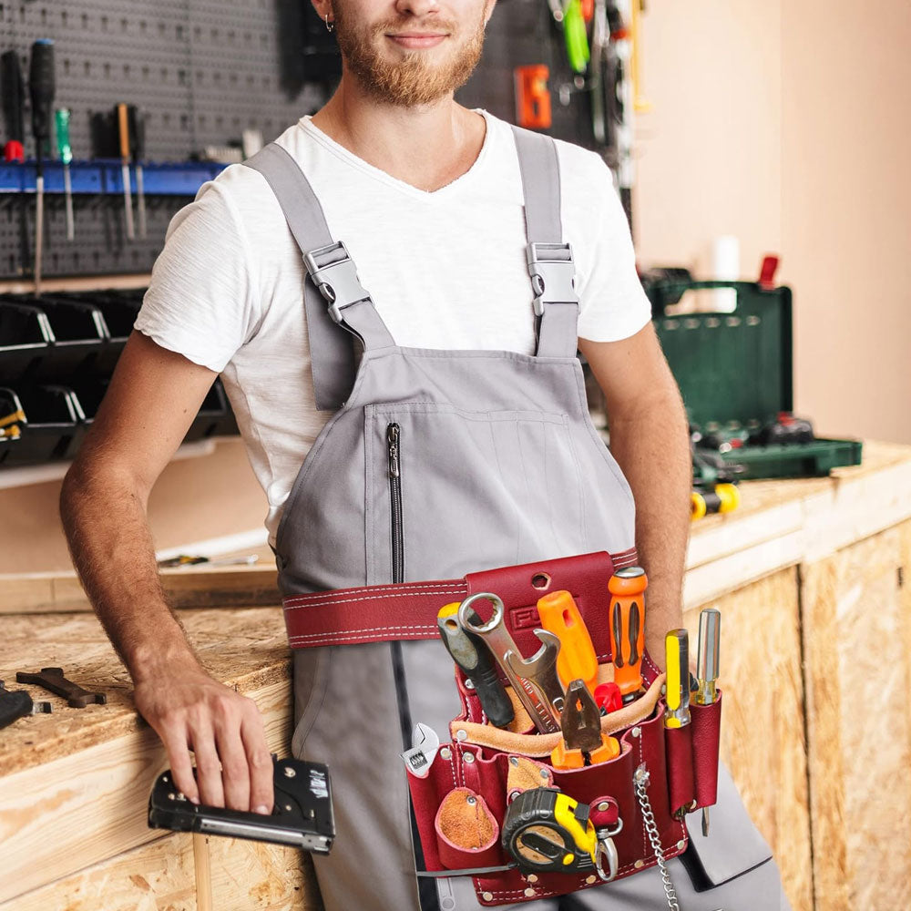 A carpenter wearing Fueri maroon leather tool pouch full of all tools, standing by a workbench, facing camera, smiling, a tool in his hand.